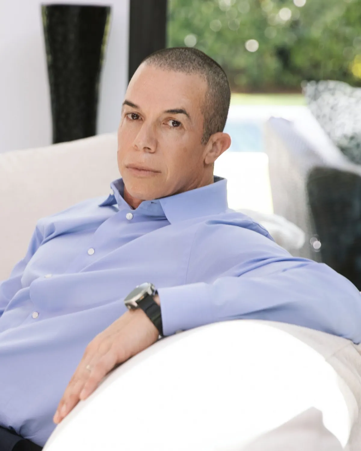 Trevor L Taylor seated on a pale sofa in a blue dress shirt, one arm resting along the back